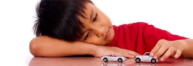 A young boy is playing with two toy cars on a table.